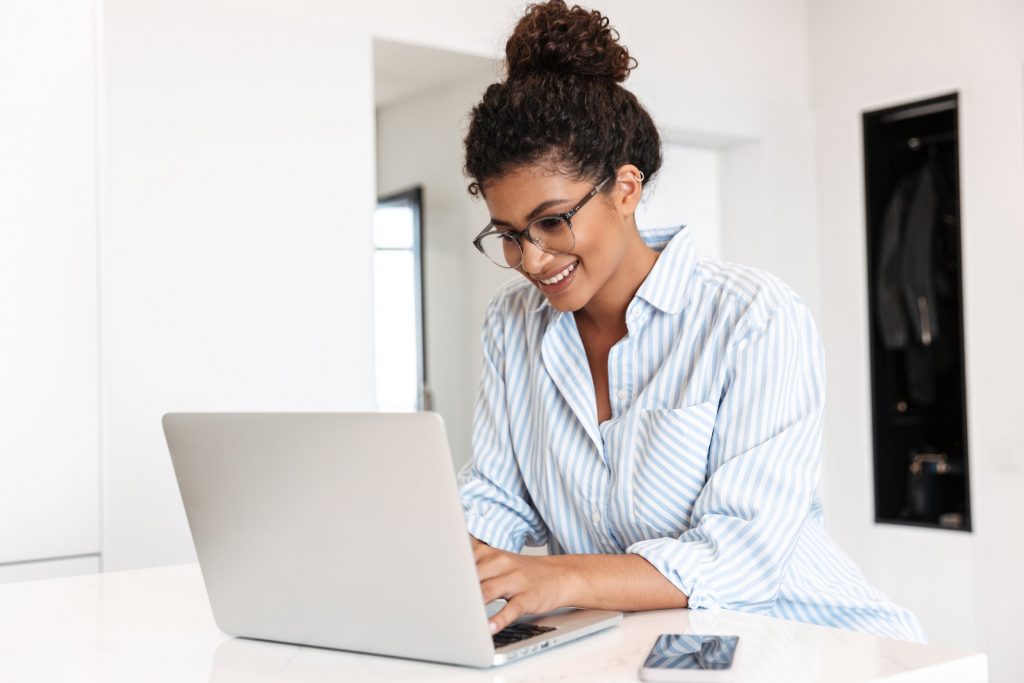 Attractive smiling young african woman working on laptop computer at the table at home